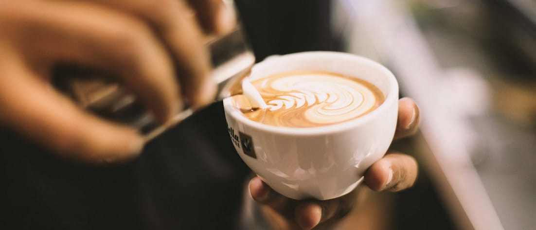 Ein Barista gießt Milchschaum in eine Tasse Cappucino