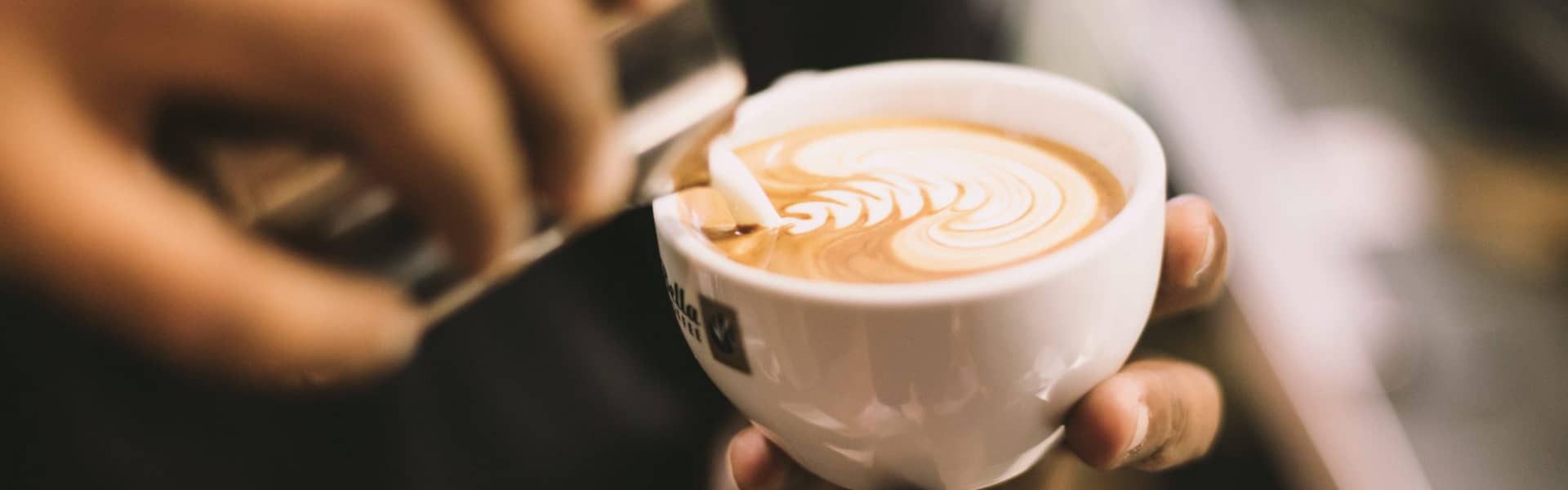 Ein Barista gießt Milchschaum in eine Tasse Cappucino