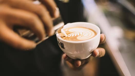 Ein Barista gießt Milchschaum in eine Tasse Cappucino