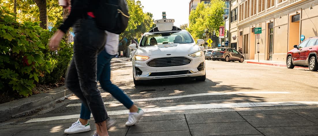 Ein autonomes Auto mit Radar-Aufbau fährt auf einen Fußgängerüberweg zu